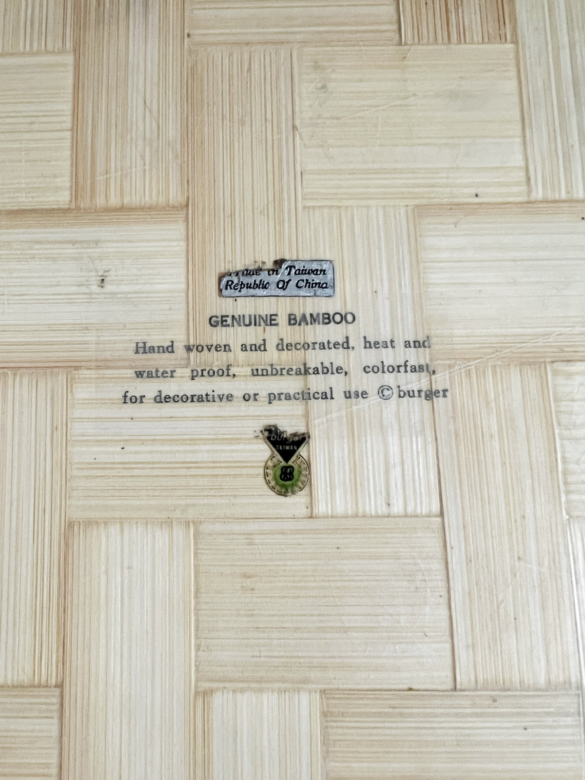 A close-up of a light natural bamboo surface with visible grain and a small printed label reading 'Genuine Bamboo' with additional text and a small badge.